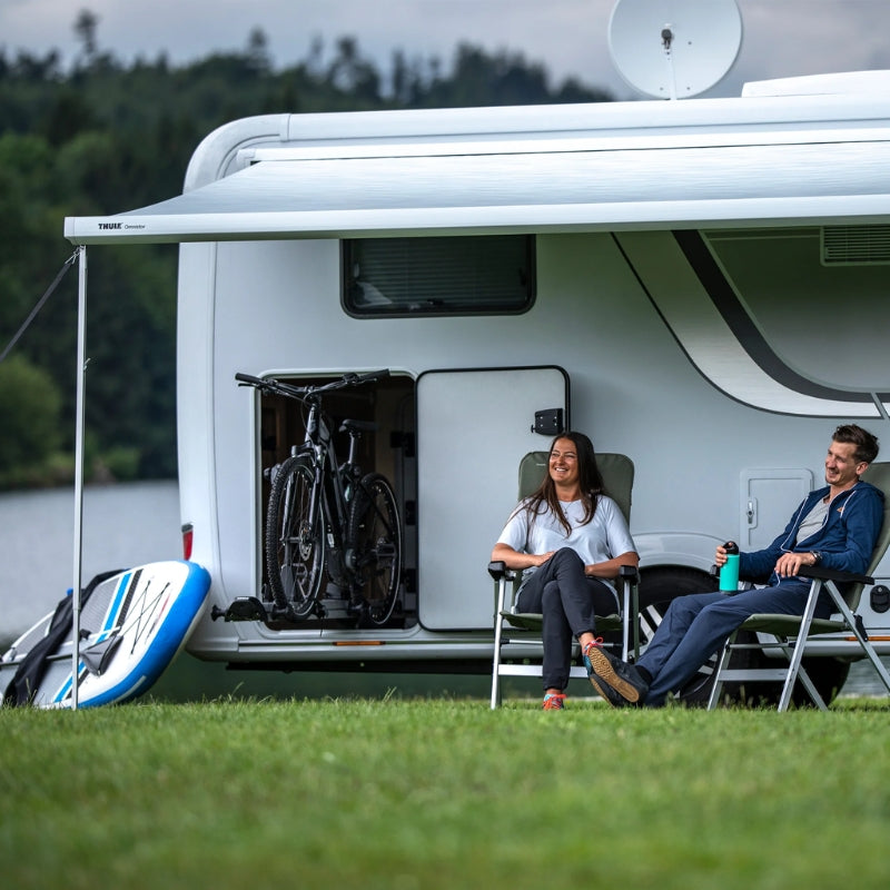 Two people by a white van in a grassy field with mountains in the background