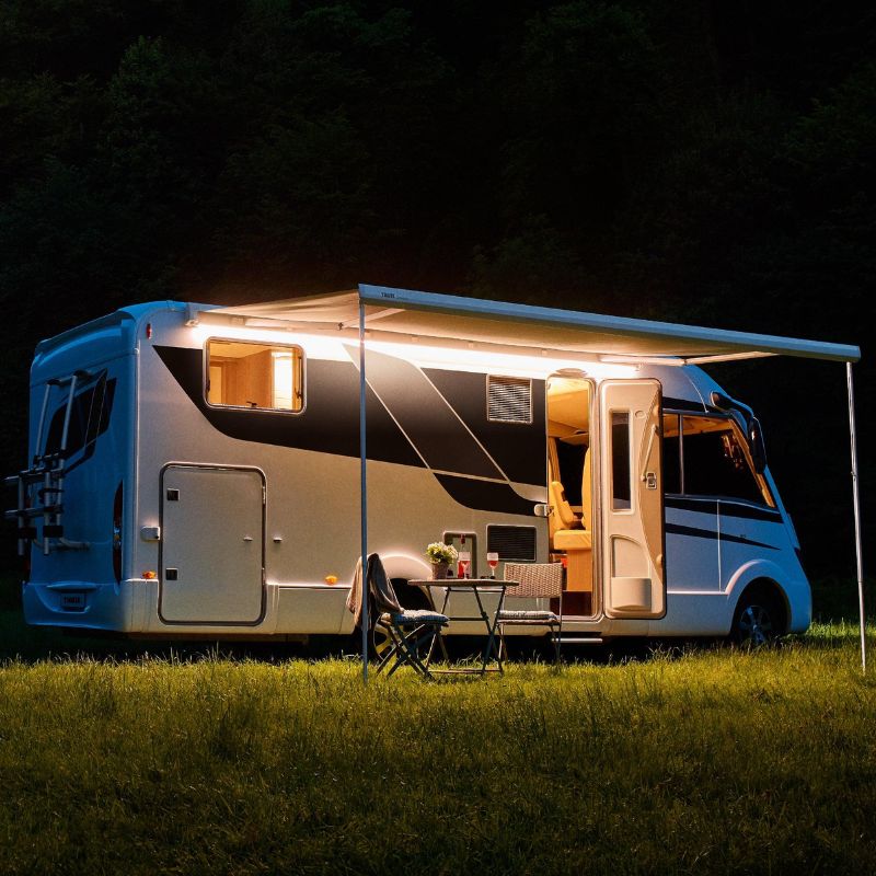 Camper van parked at night with extended awning, outdoor table and chairs set up beside the RV